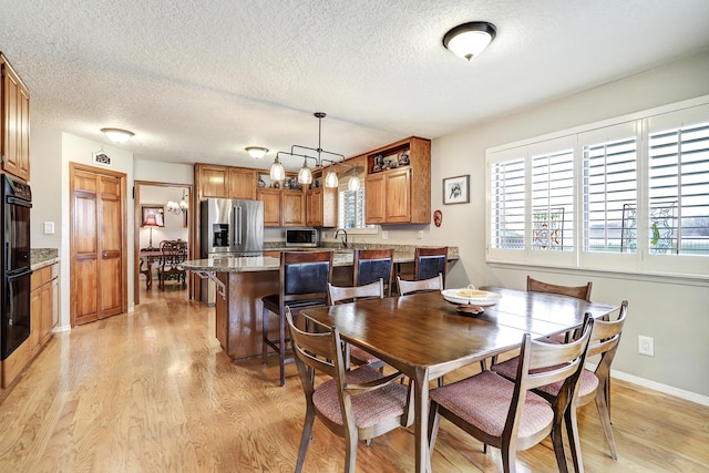 dining space with light wood-style floors, baseboards, a textured ceiling, and an inviting chandelier