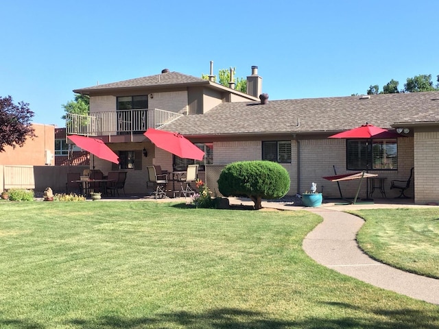 rear view of house with a balcony, brick siding, and a yard