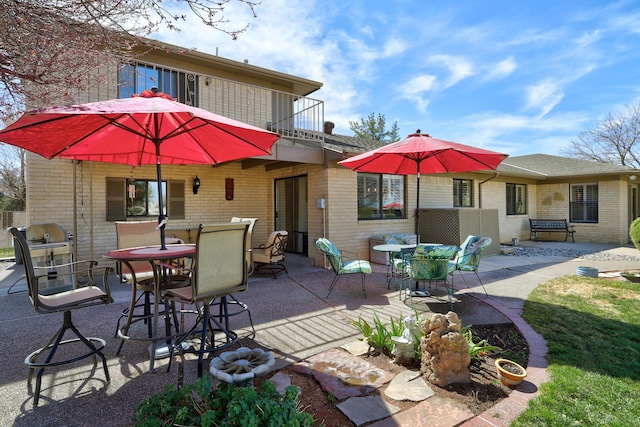 rear view of property with brick siding, outdoor dining area, a patio area, and a balcony