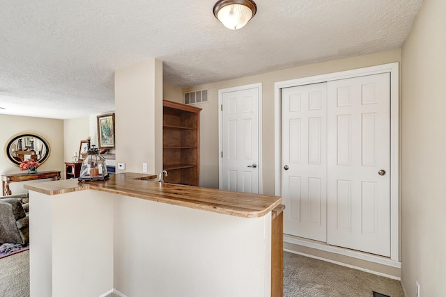 kitchen featuring carpet floors, visible vents, a peninsula, and a textured ceiling