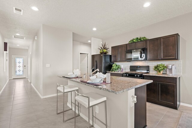 kitchen featuring dark brown cabinetry, visible vents, decorative backsplash, black appliances, and a kitchen bar