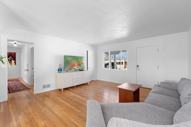 living room with light wood-type flooring, visible vents, and baseboards