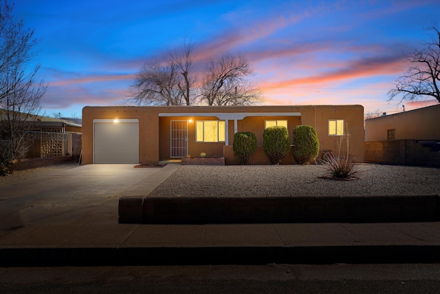 view of front of property featuring a garage, driveway, fence, and stucco siding