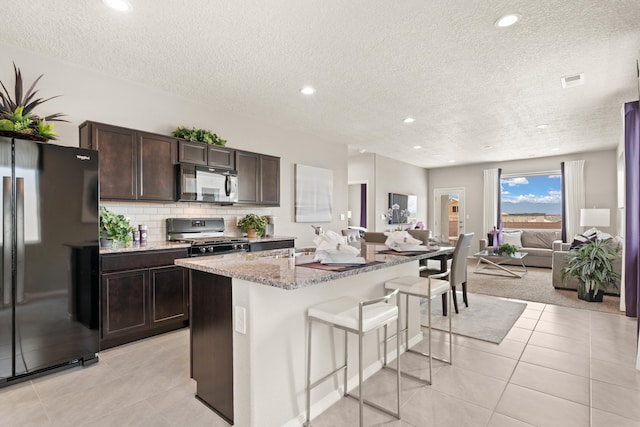 kitchen featuring open floor plan, a breakfast bar, freestanding refrigerator, dark brown cabinets, and gas stove