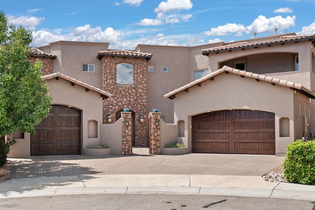 mediterranean / spanish house with a garage, stone siding, decorative driveway, and stucco siding