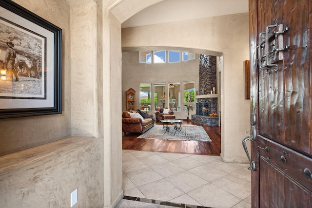 entryway featuring a towering ceiling, light tile patterned floors, baseboards, and a stone fireplace