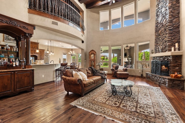 living room with arched walkways, ceiling fan with notable chandelier, a fireplace, dark wood-style floors, and beamed ceiling