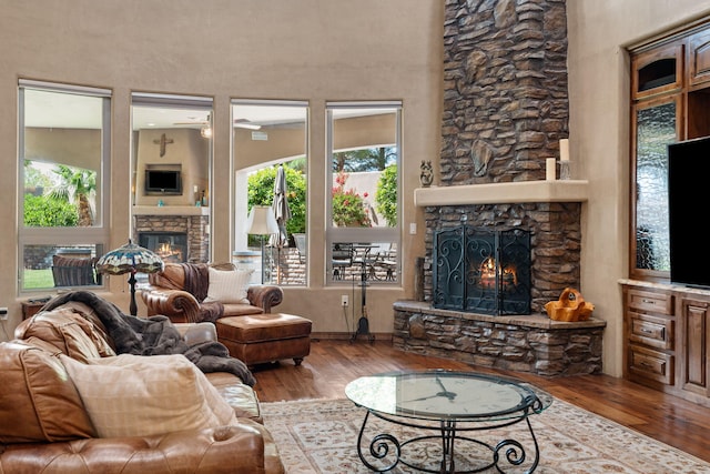 living area featuring a stone fireplace, a towering ceiling, and wood finished floors