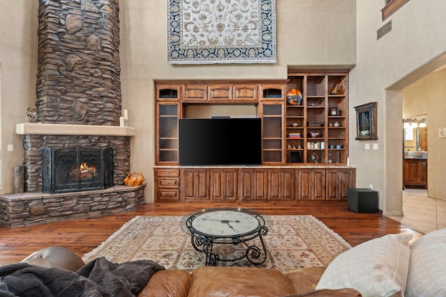 living area with visible vents, a fireplace, a towering ceiling, and wood finished floors