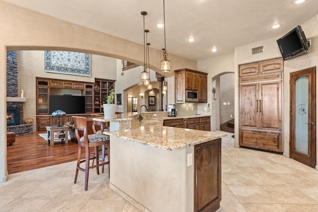 kitchen featuring arched walkways, decorative light fixtures, a sink, a peninsula, and a kitchen breakfast bar