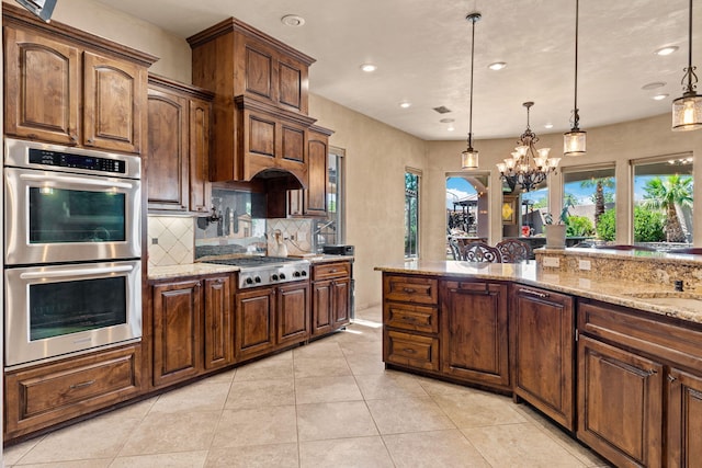 kitchen with stainless steel appliances, hanging light fixtures, backsplash, and light stone countertops