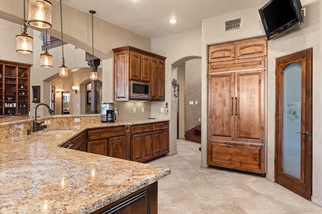 kitchen with visible vents, arched walkways, stainless steel microwave, decorative light fixtures, and a sink