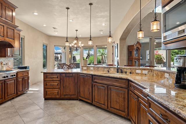 kitchen featuring light stone counters, stainless steel gas cooktop, decorative light fixtures, and a sink