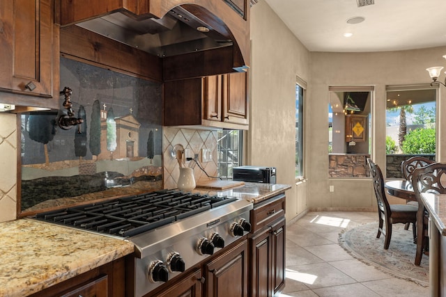 kitchen with light stone counters, light tile patterned flooring, stainless steel gas cooktop, backsplash, and custom exhaust hood