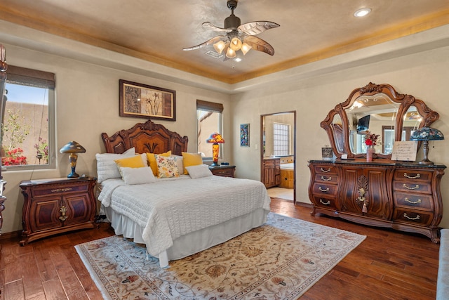 bedroom with dark wood-style floors, a raised ceiling, visible vents, and ensuite bath