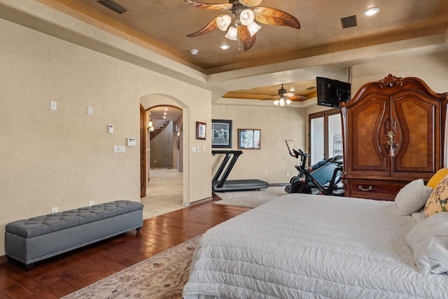 bedroom with arched walkways, wood finished floors, a raised ceiling, and visible vents