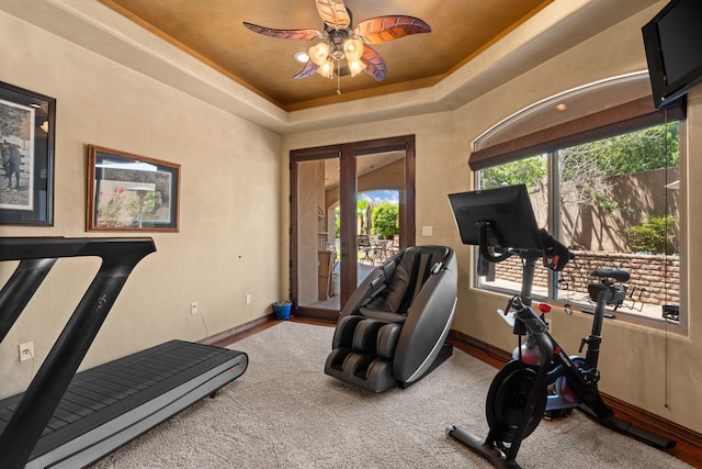 workout area with a tray ceiling, carpet flooring, ceiling fan, and baseboards