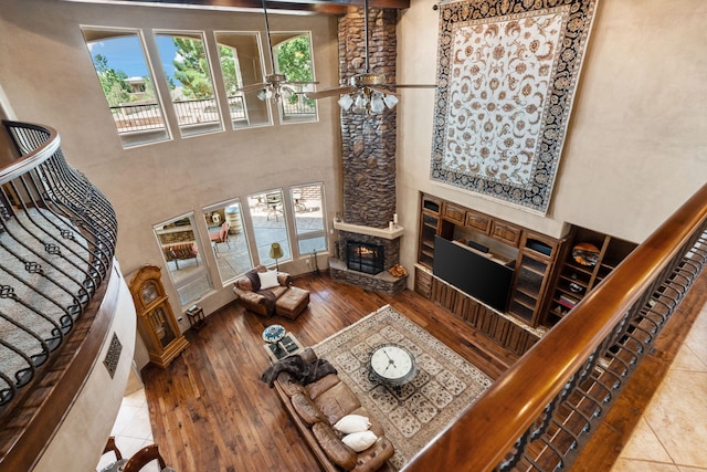 living room with stairs, a stone fireplace, a towering ceiling, and wood finished floors