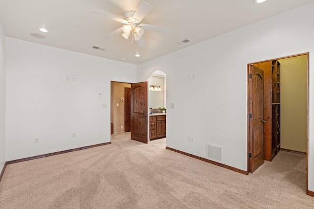 unfurnished bedroom featuring arched walkways, visible vents, light carpet, and baseboards