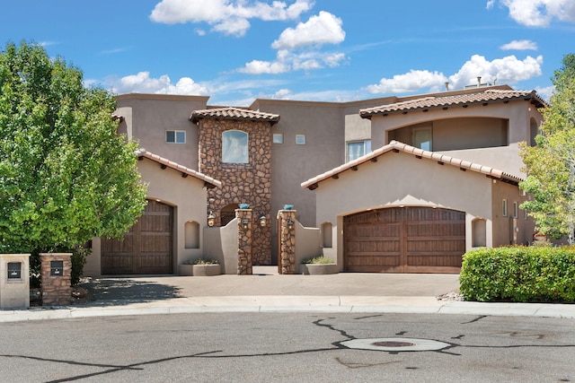 mediterranean / spanish home featuring a garage, a tile roof, driveway, stone siding, and stucco siding