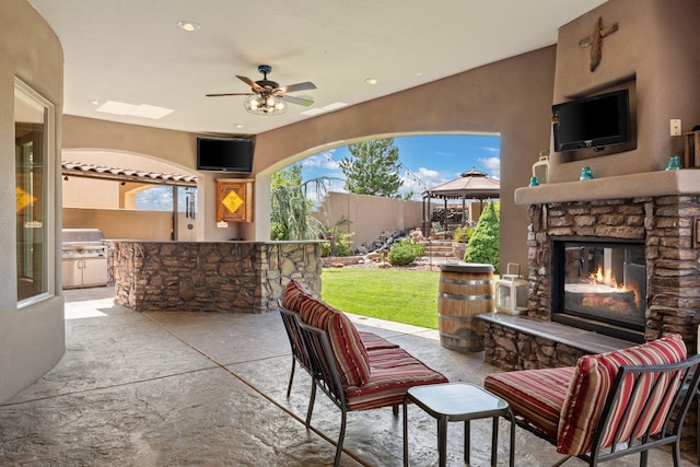 view of patio featuring an outdoor stone fireplace, grilling area, a gazebo, fence, and exterior kitchen