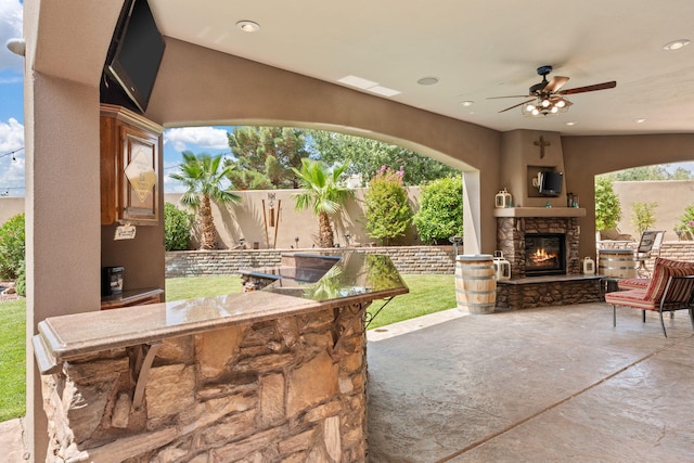 view of patio featuring an outdoor stone fireplace, an outdoor bar, ceiling fan, and fence