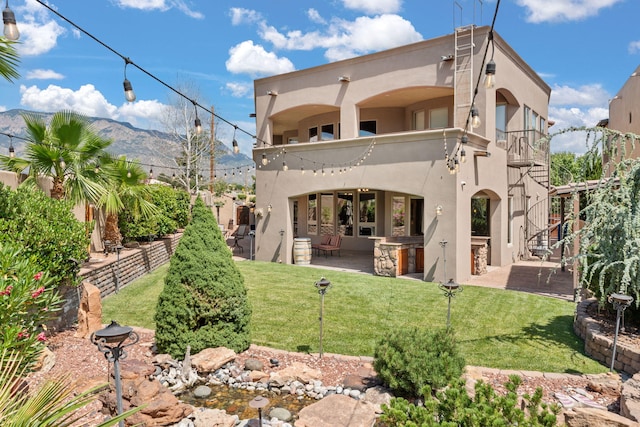 rear view of property featuring a mountain view, a balcony, exterior kitchen, stucco siding, and a patio area