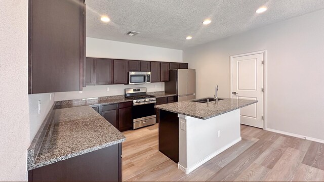 6053 Strand Loop SE, Albuquerque, NM 87106 - kitchen featuring appliances with stainless steel finishes, a sink, light wood finished floors, dark brown cabinets, and a kitchen island with sink