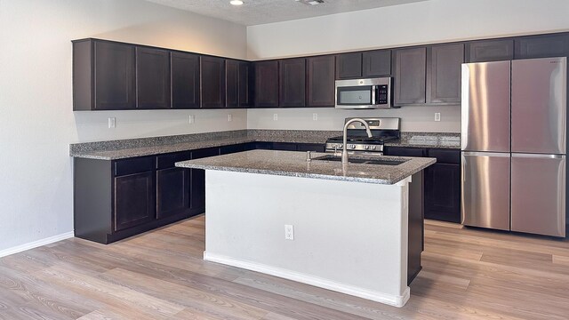 6053 Strand Loop SE, Albuquerque, NM 87106 - kitchen featuring stainless steel appliances, light wood-style floors, dark stone countertops, an island with sink, and baseboards