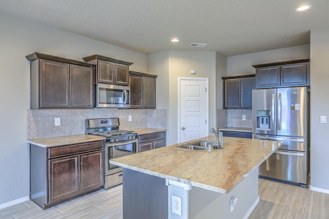 kitchen with stainless steel appliances, visible vents, a kitchen island with sink, a sink, and dark brown cabinets