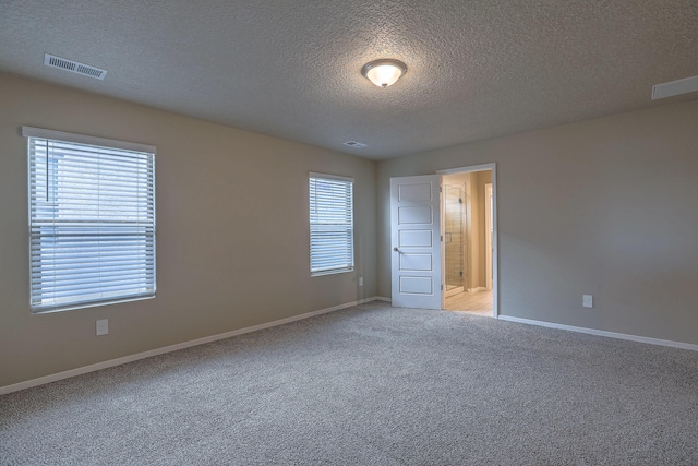 empty room with light carpet, a textured ceiling, visible vents, and baseboards