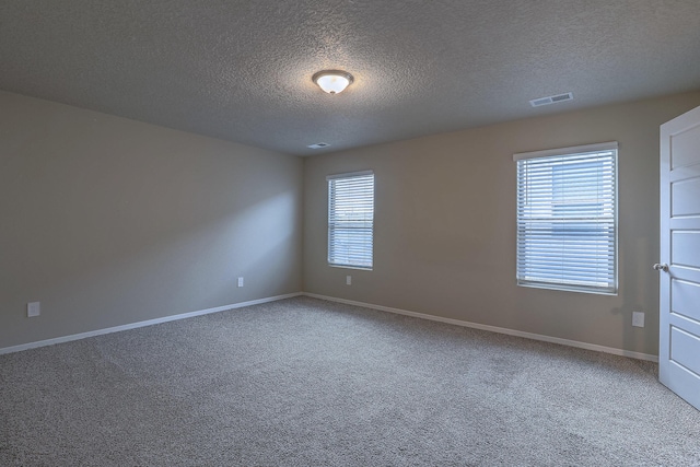 spare room with carpet floors, visible vents, a textured ceiling, and baseboards