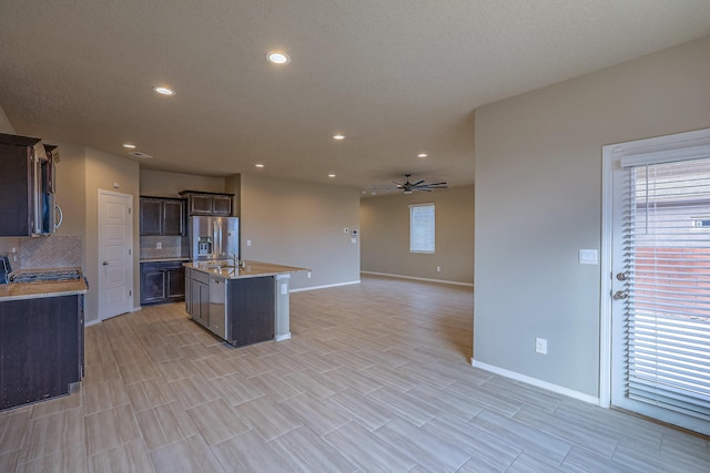 kitchen with tasteful backsplash, appliances with stainless steel finishes, open floor plan, a kitchen island with sink, and light countertops