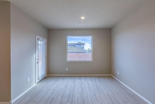 empty room with a textured ceiling, light wood-style flooring, visible vents, and baseboards