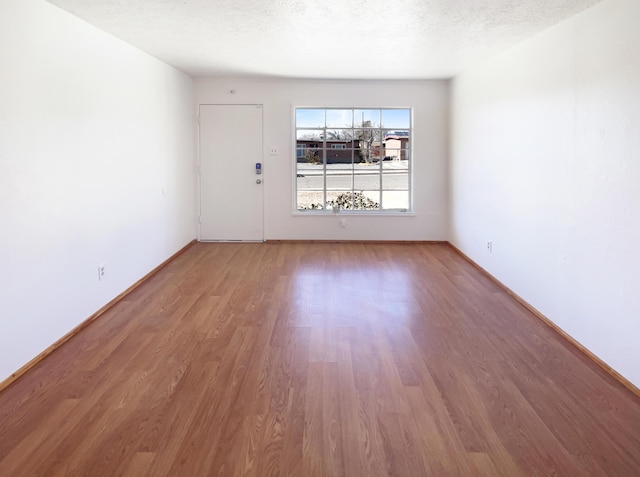 unfurnished room featuring baseboards, a textured ceiling, and wood finished floors