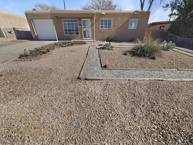 pueblo-style home featuring driveway, an attached garage, fence, and stucco siding