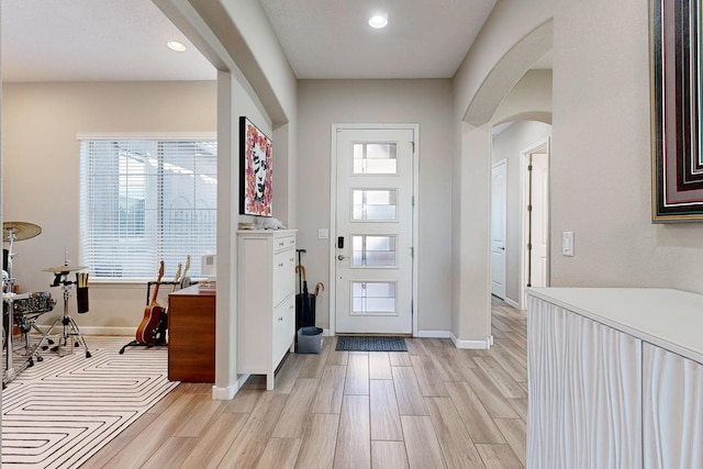 foyer featuring light wood-style flooring, recessed lighting, arched walkways, and baseboards