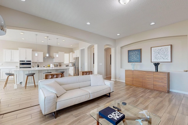 living area featuring recessed lighting, baseboards, arched walkways, and light wood-style flooring