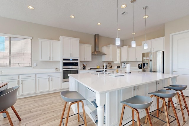 kitchen featuring white cabinetry, appliances with stainless steel finishes, a breakfast bar area, and wall chimney range hood