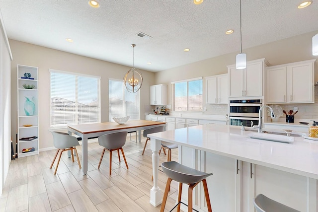 kitchen featuring visible vents, stainless steel double oven, light countertops, a kitchen bar, and backsplash