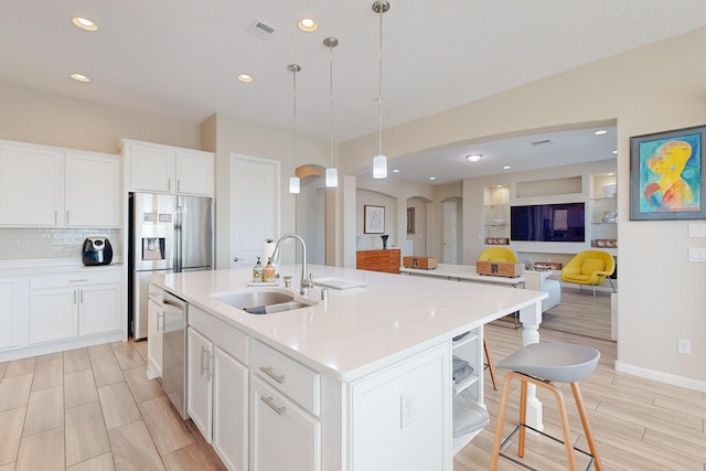 kitchen with visible vents, an island with sink, stainless steel appliances, a sink, and pendant lighting