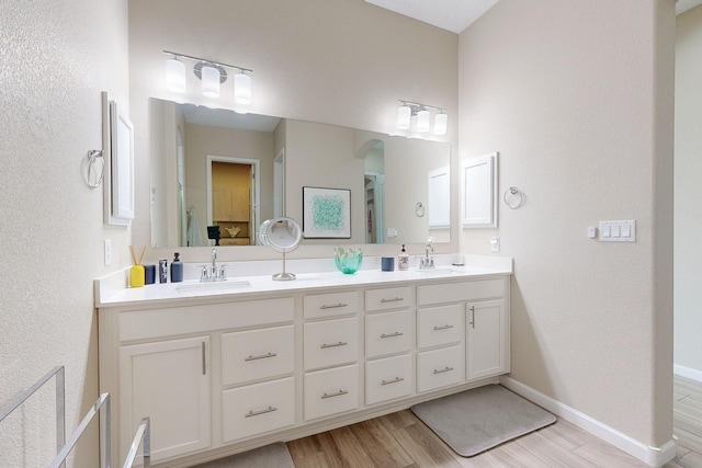 bathroom featuring double vanity, wood finished floors, baseboards, and a sink