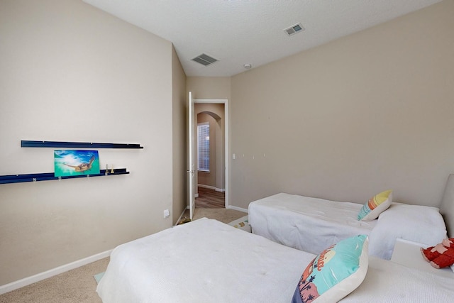 carpeted bedroom with visible vents, baseboards, arched walkways, and a textured ceiling