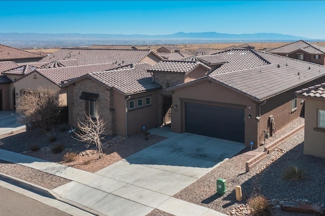 view of front of house featuring driveway, an attached garage, stucco siding, a tile roof, and a mountain view