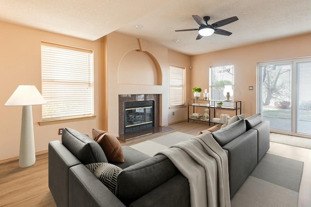 living area with light wood-style flooring, a premium fireplace, a ceiling fan, and a textured ceiling