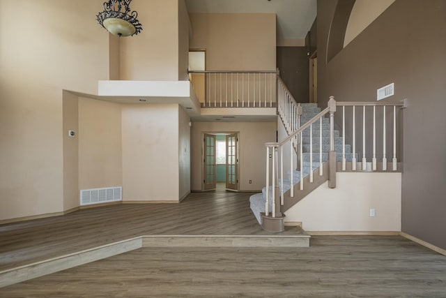 interior space with a towering ceiling, baseboards, visible vents, and wood finished floors