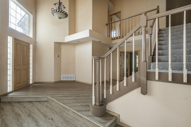 foyer entrance with a high ceiling, wood finished floors, visible vents, baseboards, and stairway