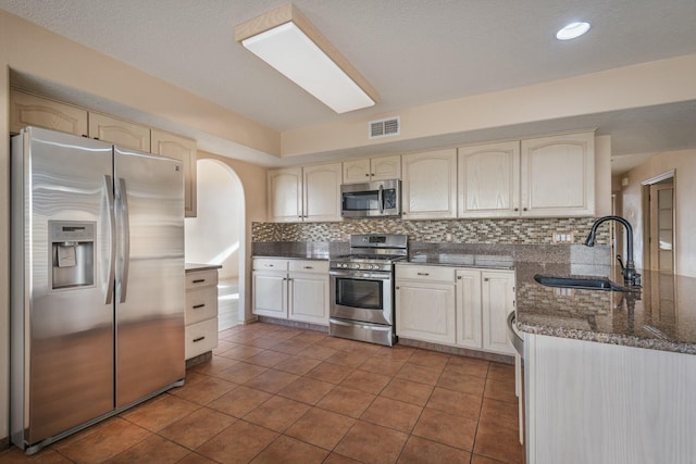 kitchen featuring tasteful backsplash, visible vents, appliances with stainless steel finishes, a sink, and a peninsula