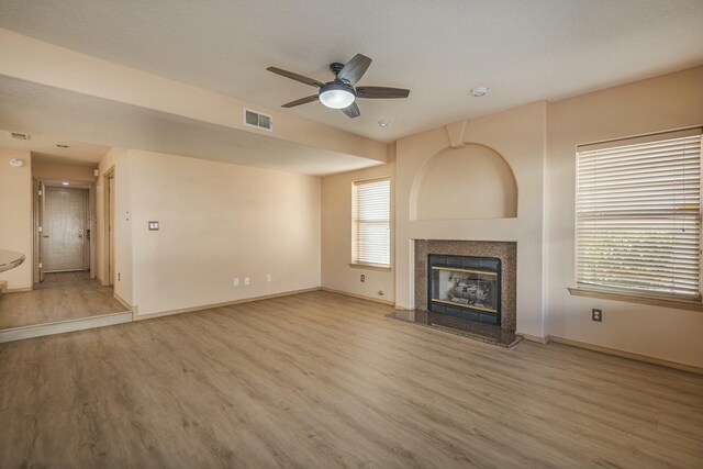 unfurnished living room featuring ceiling fan, a fireplace, visible vents, and wood finished floors