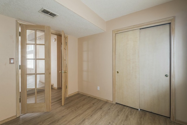 unfurnished bedroom featuring baseboards, visible vents, a textured ceiling, light wood-type flooring, and a closet